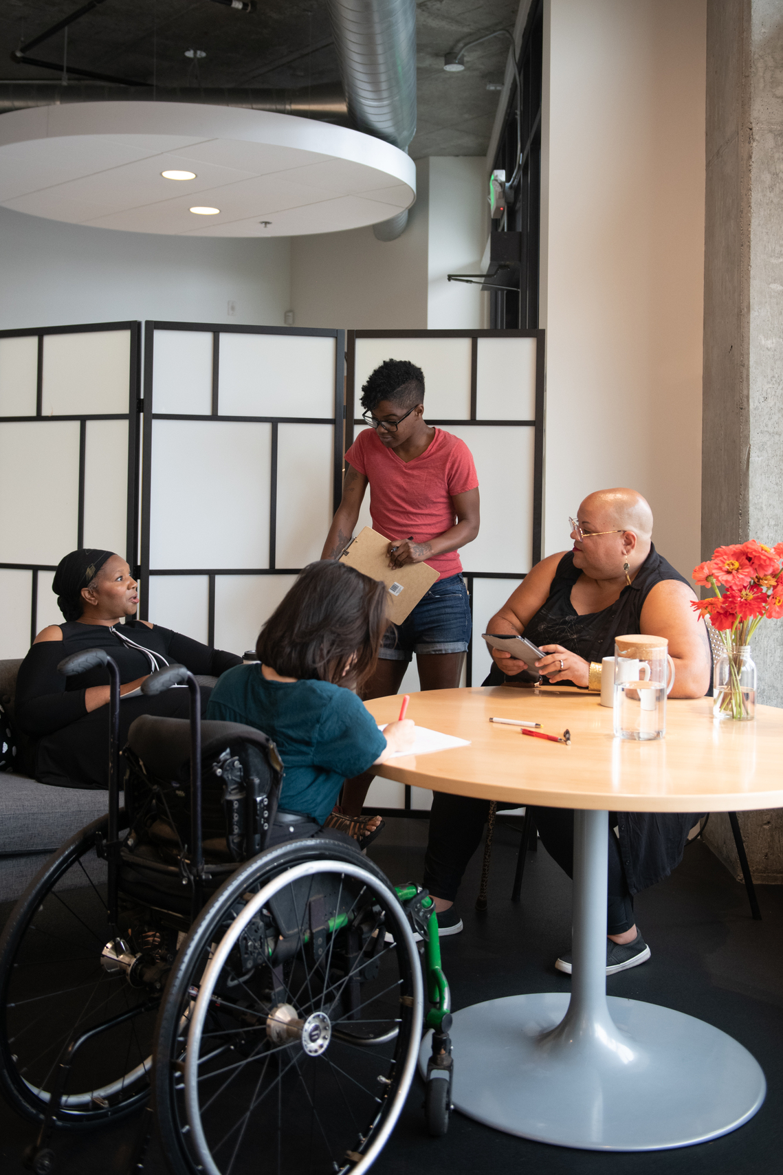 A group of black women having a discussion around a table, in an office setting. Image courtesy of Disabled and Here